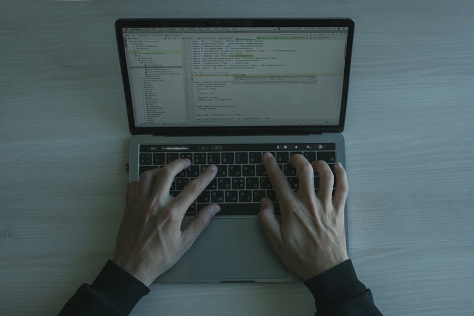 Person typing code on a laptop, representing exploit paths turning bugs into takeovers
